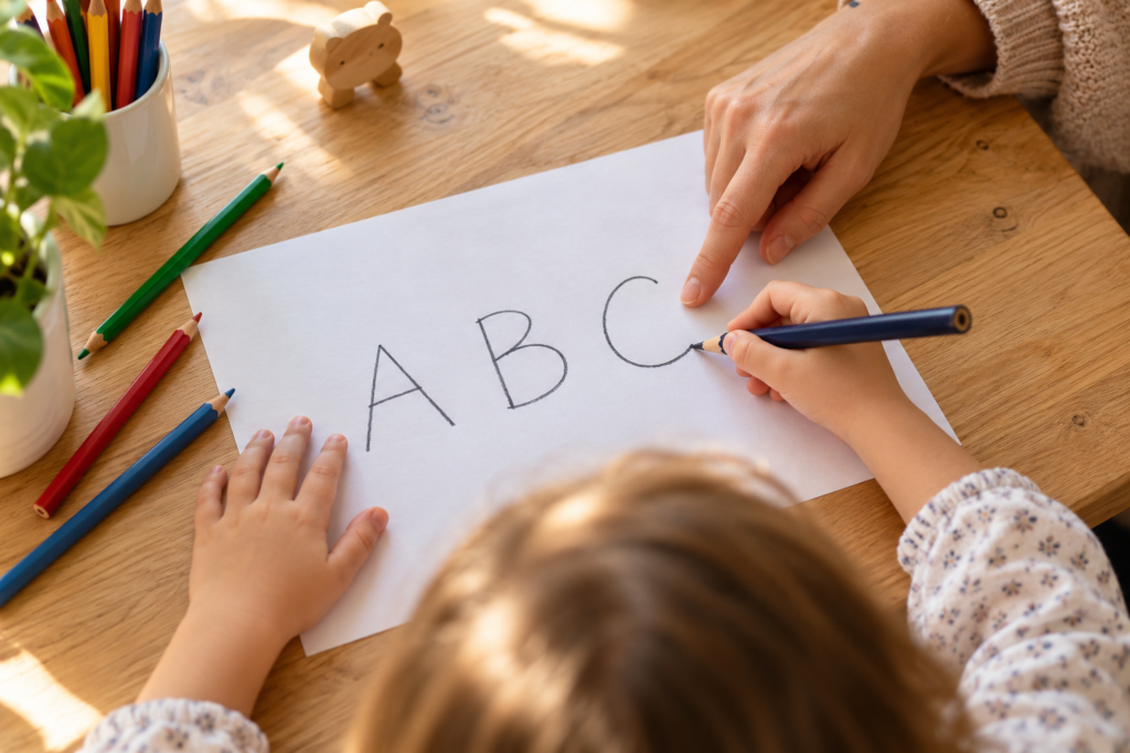 Child practicing the letters A, B and C on paper with a parent’s guidance.